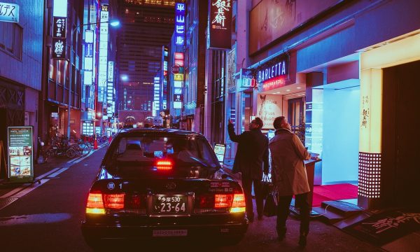 雨夜街道的霓虹倒影，一位撑伞的行人走过积水路面，画面偏蓝紫，典型的日韩都市电影氛围